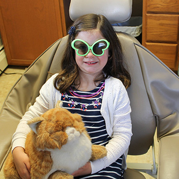 girl in dentist chair with sunglasses and stuffed animals